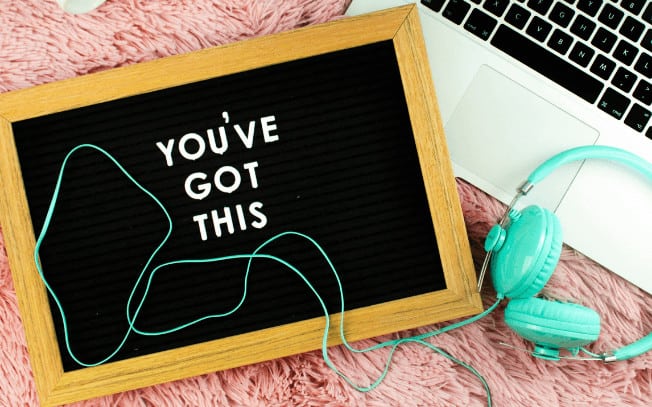 A sign that says "you've got this" with teal headphones and laptop styled on a pink carpet