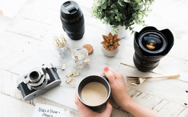 birds-eye view of hands holding a cup of coffee with camera lenses and a plant.