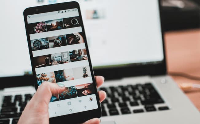 Hand holding a cell phone in front of a laptop